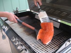 Ein Lachs wird auf einem Gasgrill gewendet.