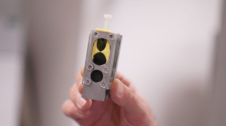 Protoyp einer Bakterien-Batterie | Bildquelle: P. Bombelli Etwa handtellergroßes metallenes Kästchen mit einem grünen Innenraum, der durch drei Öffnungen zu sehen ist