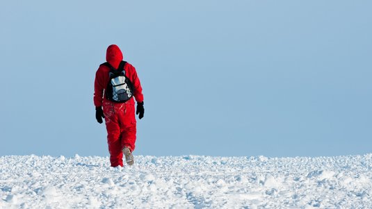 Mann mit Rucksack in einer menschenleeren Schneelandschaft
