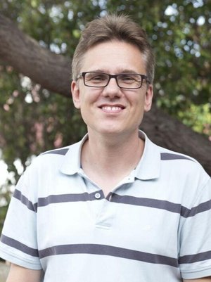 Das Bild zeigt den Wissenschaftler Michael Küppers, der ein gestreiftes T-Shirt trägt und vor einem Baum steht. 