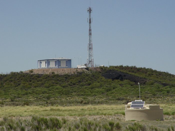 Im Vordergrund ist ein Wasser-Tscherenkow-Detektor zu sehen, im Hintergrund auf einer leichten Anhöhe ein Teleskopgebäude.