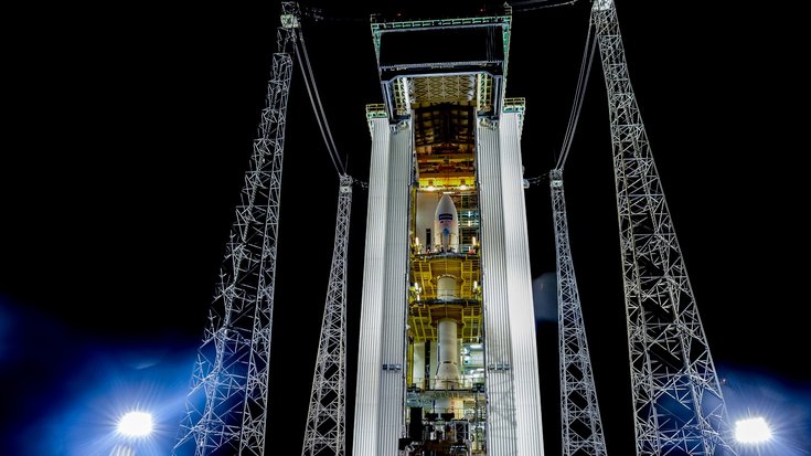 Raketenrampe mit Satelliten angestrahlt von Lampen vor dem Nachthimmel.