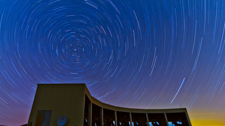 Gebäude mit vielen Teleskopen, darüber der Nachthimmel mit Sternspuren.
