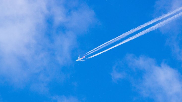 Blauer Himmel, über den ein Flugzeug fliegt, an dessen hinterem Ende sich ein Kondensstreifen zeigt.