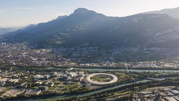 Das Bild zeigt eine Stadt, Berge, einen Fluss und einen großen Beschleunigerring.