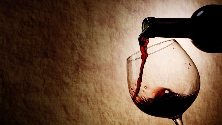 Aus einer Flasche wird Rotwein in ein Glas eingeschenkt