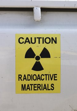 Gelbes Warnschild mit Symbol für Radioaktivität auf einer Metallwand.