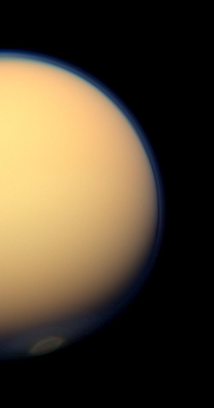 Saturnmond Titan Gelb-orange ragt der Saturnmond als große Halbkugel in das Bild. Die Dunstschicht hebt sich als blaue Hülle um den Mond vor dem schwarzen Hintergrund ab.