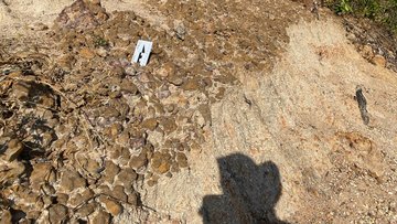 Krater in einer Erdschicht, im Vordergrund ein Schatten der fotografierenden Person