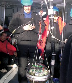 Personen in dicker Winterkleidung hinter einer durchsichtigen Kugel mit Elektronik im Inneren. Die Kugel hängt an einer Halterung.