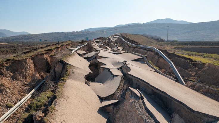Abilgebildet ist eine Straße, die durch ein Erdbeben zerstört wurde. Die Fahrbahn ist durch längliche Risse zerstört.