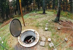 Foto. Diverse Messgeräte auf Waldboden. Im Vordergrund Öffnung eines Schachts.