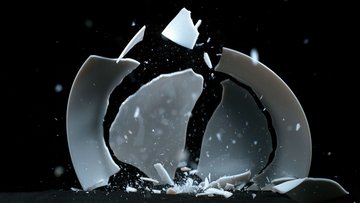 Das Bild zeigt den Moment, in dem ein Teller mit der Kante auf den Boden fällt und in größere und kleinere Bruchstücke zersplittert.