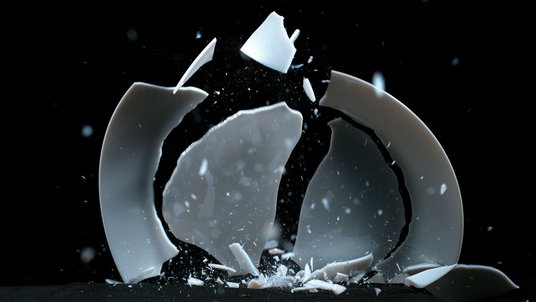 Das Bild zeigt den Moment, in dem ein Teller mit der Kante auf den Boden fällt und in größere und kleinere Bruchstücke zersplittert.