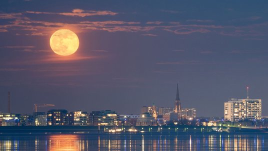 Großer, tiefstehender Vollmond über einer Hafenstadt