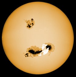 Ein Stern mit zwei Flecken, der untere ist deutlich größer als der obere, er zeichnet sich nicht nur als schwarzes Loch von der Oberfläche des Sterns ab, das ausgestoßene Gas leuchtet auch noch weiß auf.