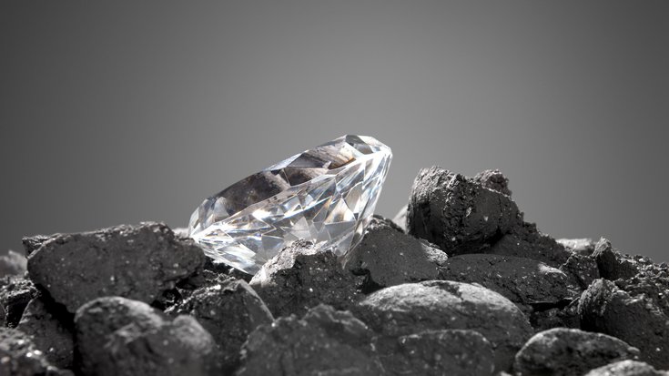 Auf dunklen Steinen liegt ein geschliffener Diamant.