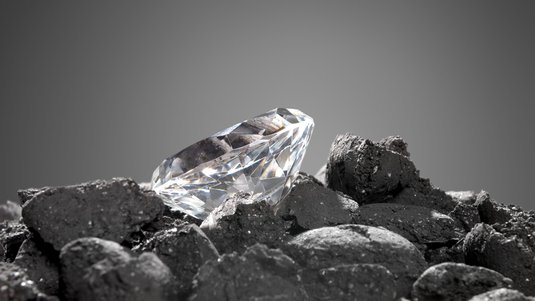 Auf dunklen Steinen liegt ein geschliffener Diamant.