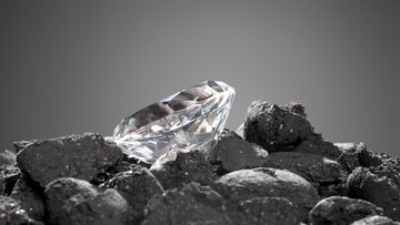 Auf dunklen Steinen liegt ein geschliffener Diamant.