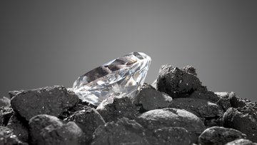 Auf dunklen Steinen liegt ein geschliffener Diamant.