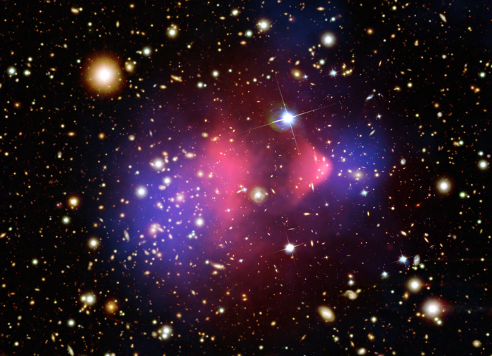 Indirekter Nachweis von Dunkler Materie Viele Galaxien vor schwarzem Hintergrund. In der Mitte befindet sich ein hantelfömiger, rosa Klumpen, an dessen beiden Seiten ein blauer Klumpen angrenzt.