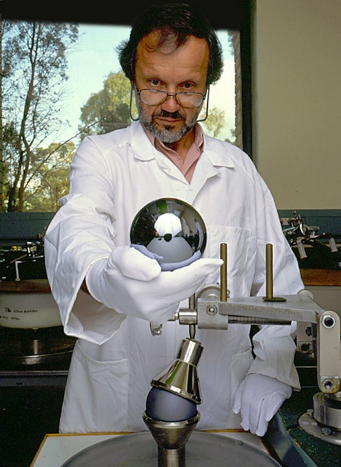 Siliziumkugel für das Avogadro-Projekt In einem Labor hält ein Mann im weißen Kittel und mit weißen Stoffhandschuhen hält eine metallisch-spiegelnde Siliziumkugel von etwa zehn Zentimetern Durchmesser in der Hand.