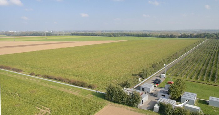 Detektor GEO600 Das Bild zeigt Gebäude, das aus mehreren Containern besteht und von Feldern umgeben ist. Es gehen zwei Kanäle im rechten Winkel von den zentralen Gebäuden ab.