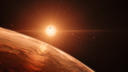 Im Vordergrund ein Teil eines Planeten, im Hintergrund ein rötlicher Stern mit sechs weiteren Planeten.