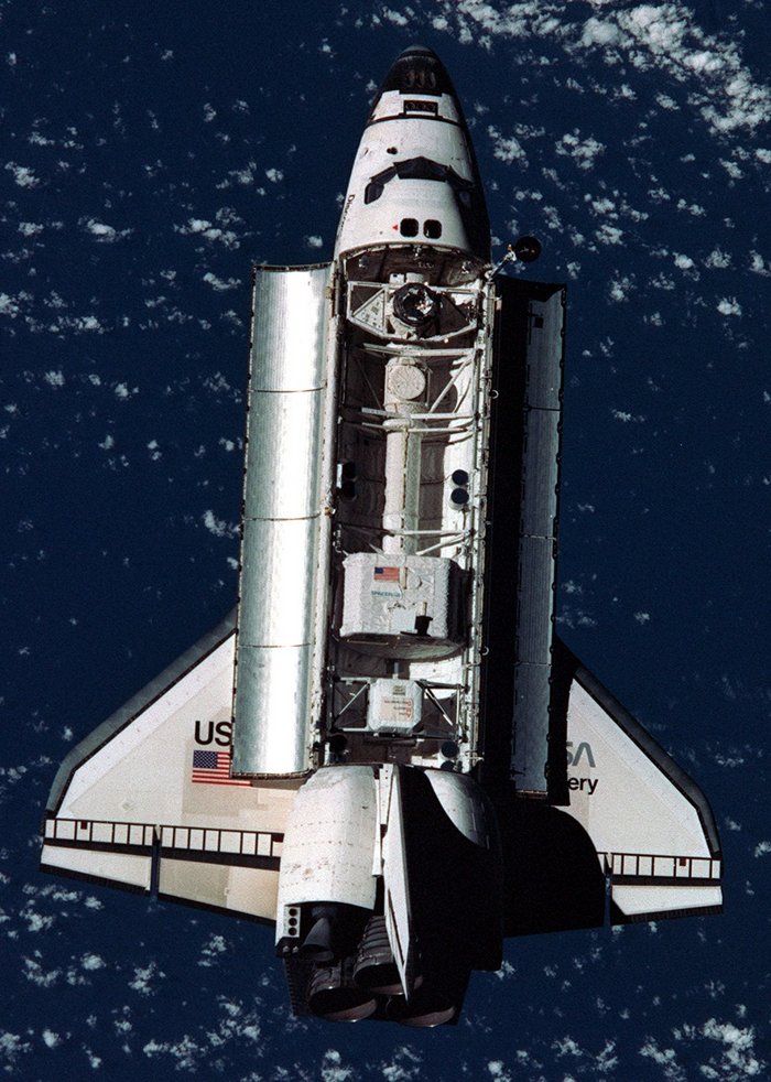 AMS-01 auf dem Testflug Die offene Ladeluke eines Space Shuttle im Weltraum über der Erde offenbar mehrere Gerätschaften im Inneren.