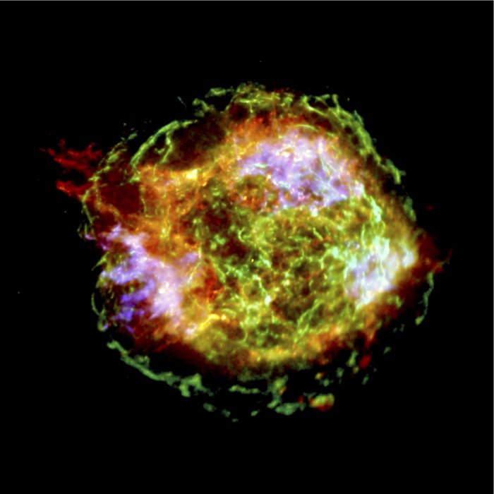 Gammastrahlenquelle: Der Supernova-Überrest Cassiopeia A Vor dunklem Hintergrund ein recht transparente Wolke in Blau, Violett und Weiß. Wolke im Innern mit weißen Nebelfetzen stark strukturiert – im Zentrum ein schwacher Stern.