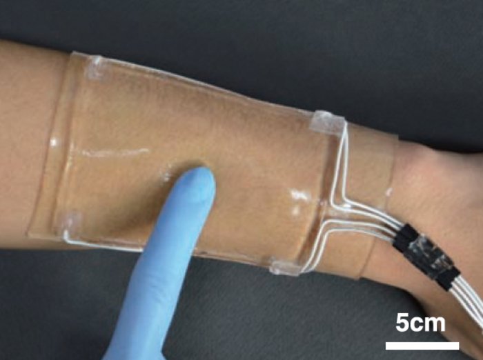 Dehnbares Touchpad Ein Touchpad aus transparenter Kunststoff, das mit Kabeln verbunden ist, ist an einem Arm angebracht. Dieser lässt sich mit einem Finger bedienen.