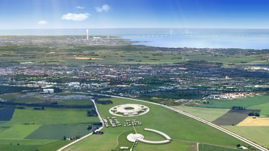 Landschaft mit Gebäuden auf einer grünen Wiese, im Hintergrund eine Stadt und eine große Brücke