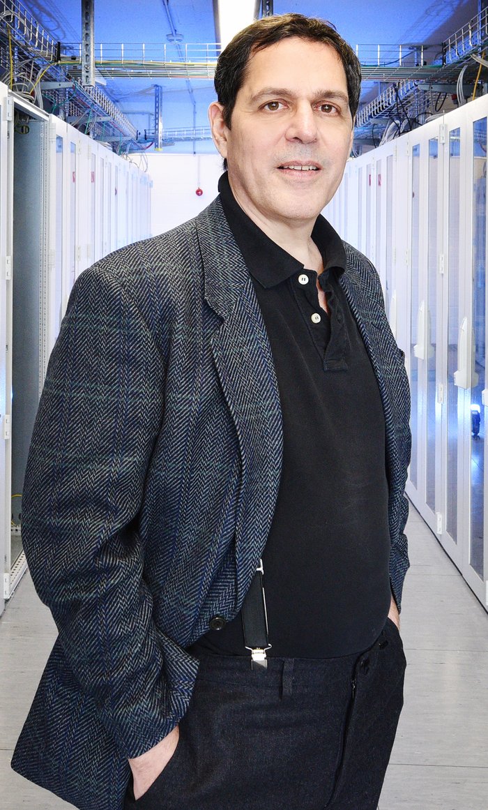 Bruce Allen Aufnahme von Bruce Allen in einem Gang mit Kabeln und Computerteilen an den Wänden.