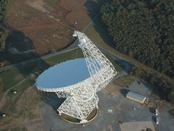 Luftaufnahme des Radioteleskops. Das Teleskop gleicht einer großen, auf einem Stahlgerüst gelagerten Schüssel. Seitlich ist ein über die Schüssel ragender Arm angebracht.