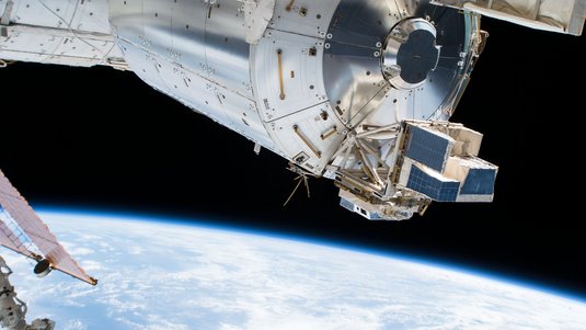 Blick von der ISS auf ein technisches Modul an der Raumstation, im Hintergrund die Erde
