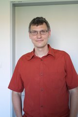 Sebastian Nauerth ist ein Mann Anfang dreißig mit kurzen, dunklen Haaren. Er trägt ein kurzärmeliges, rotes Hemd und eine unauffällige Brille.