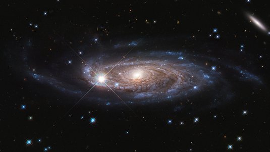 Aufnahme einer Spiralgalaxie: Ein heller, gelblich-weißer Kern wird von bläulichen Spiralarmen umhüllt. 