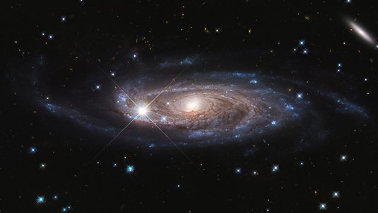Aufnahme einer Spiralgalaxie: Ein heller, gelblich-weißer Kern wird von bläulichen Spiralarmen umhüllt. 
