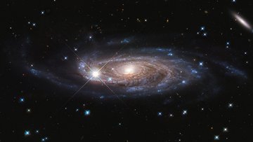 Aufnahme einer Spiralgalaxie: Ein heller, gelblich-weißer Kern wird von bläulichen Spiralarmen umhüllt. 