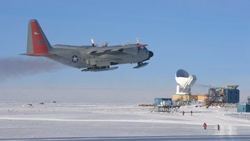 Ein Frachtflugzeug im Tiefflug, im Hintergrund wissenschaftliche Installationen mit drei senkrecht nach oben gerichteten Parabolantennen