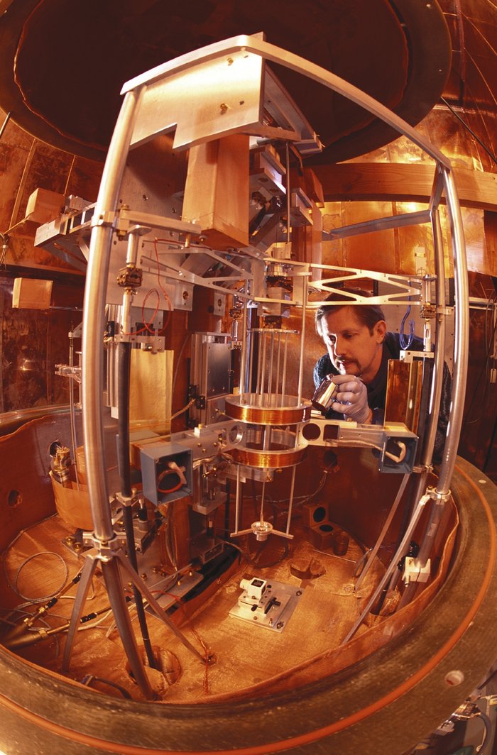 Die Watt-Waage des NIST Fischaugen-Foto der Watt-Waage aus Metallstreben, Kabeln und Spulen. Ein Forscher stellt eine Kopie des Ur-Kilogramms hinein.
