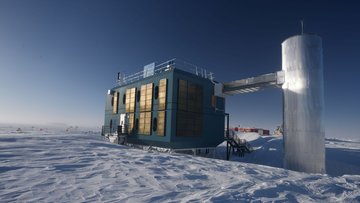Containerartiges Gebäude mit einem Geländer auf dem Dach steht in einer Schneelandschaft. Es ist verbunden mit einer vertikal aufgerichteten silbernen Röhre, die ungefähr so hoch ist wie das Haus