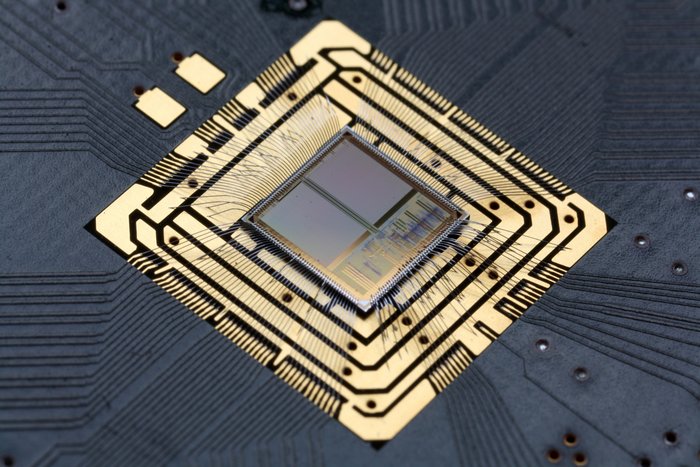 Foto eines neuromorphen Chips Ein quadratischer, metallisch glänzender Chip, auf dem feingliedrige Strukturen zu erkennen sind.