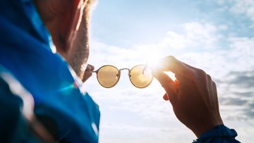 Mann hält Sonnenbrille vor seine Augen der Sonne entgegen