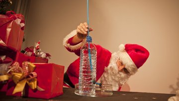 Ein Mann im Weihnachtsmannkostüm hält ein Röhrchen in eine Wasserflasche und beobachtet diese.