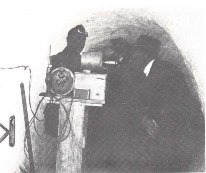 Schwarzweiss-Foto: zwei Männer vor einer technischen Messaparatur in einem Tunnel.