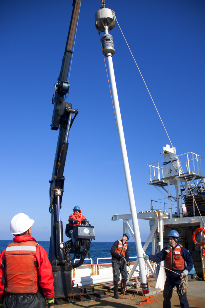Männer auf einem Schiff heben eine Metallröhre an Bord, mit der sie Sedimentproben vom Meeresboden genommen haben