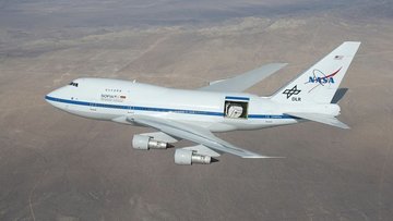 SOFIA fliegt mit offener Teleskoptür hinter der Tragfläche über eine  Wüste.