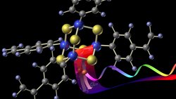 In der computergenerierten Grafik ist der Kern des Moleküls aus Zinn und Schwefel farbig gekennzeichnet, die Kohlenstoffverbindungen außen sind in grau und hellblau dargestellt. Das Licht des einfallenden Infrarotlasers ist rot und fällt auf ein bewegtes oranges Elektron, das anschließend weißes Licht abstrahlt, das als ein Band in Regenbogenfarben dargestellt ist. 
