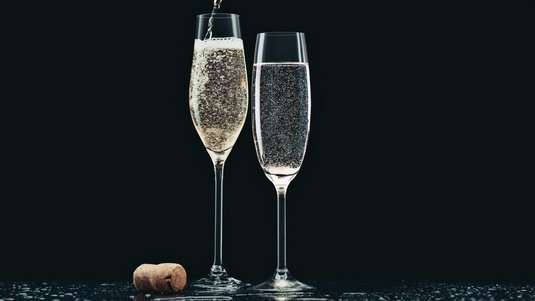 Zwei Champagnergläser; in eines davon wird das Getränkt gerade aus einer Flasche eingschenkt 